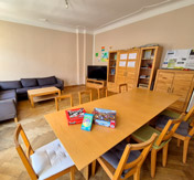 Aufenthaltsraum mit Tisch und Brettspielen, Sofa, Schränken und Regalen, sowie einem Fernseher