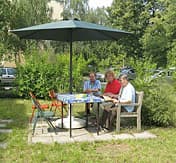 3 Männer und Frauen an einem Gartentisch unter einem SonnenschirmGartentisch 